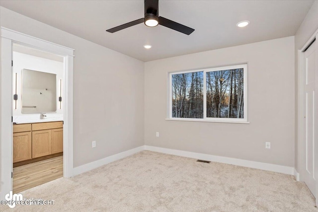 unfurnished bedroom featuring connected bathroom, sink, light colored carpet, and ceiling fan