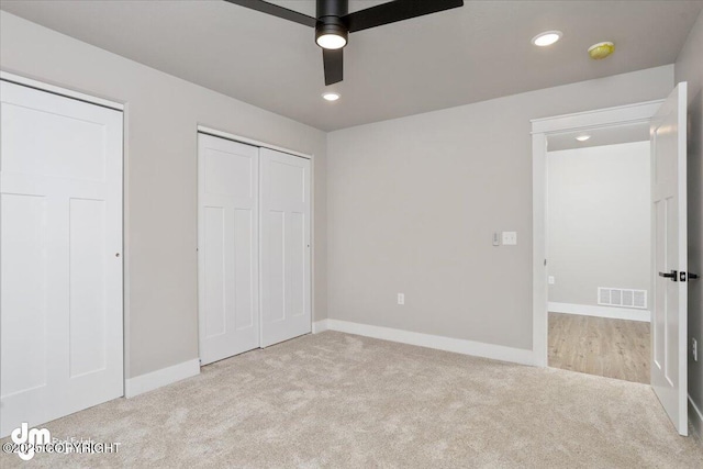 unfurnished bedroom featuring multiple closets, light carpet, and ceiling fan