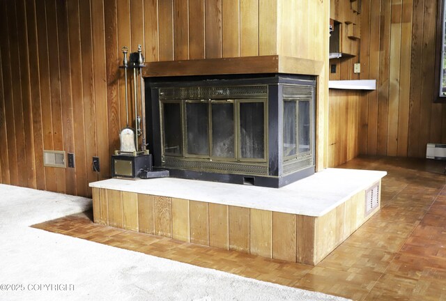 room details featuring a multi sided fireplace, a baseboard radiator, parquet floors, and wooden walls