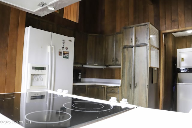 kitchen with stacked washer and dryer, white refrigerator with ice dispenser, and wood walls