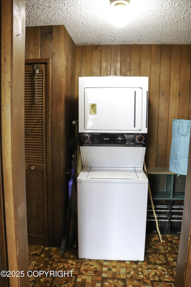 laundry room with stacked washing maching and dryer, wood walls, and a textured ceiling