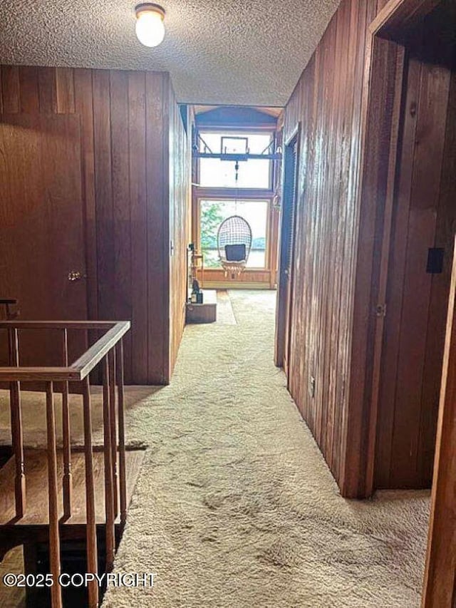 corridor with carpet floors, a textured ceiling, and wooden walls