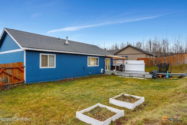 back of house with a trampoline, a yard, and a wooden deck