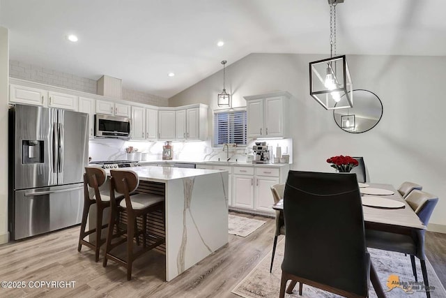 kitchen featuring white cabinets, a kitchen island, decorative light fixtures, stainless steel appliances, and vaulted ceiling