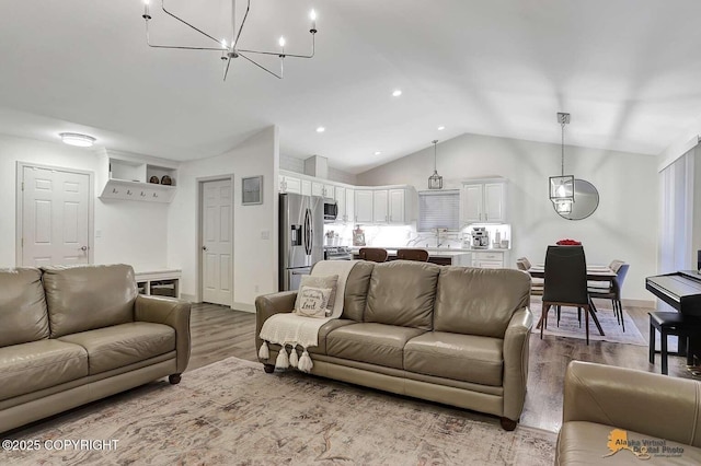 living room with hardwood / wood-style floors, a notable chandelier, and vaulted ceiling