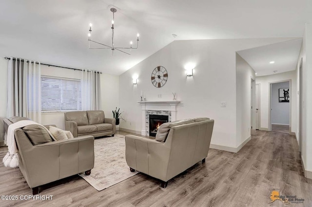 living room featuring light hardwood / wood-style floors, a chandelier, lofted ceiling, and a premium fireplace