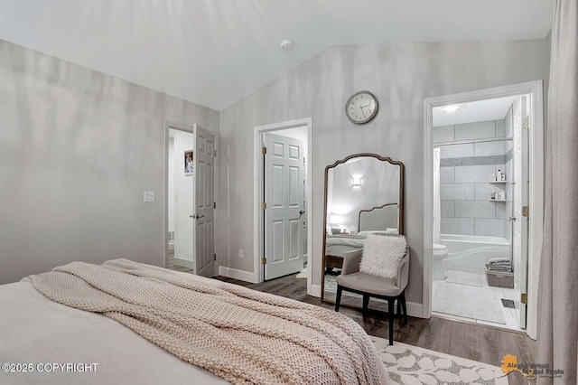 bedroom with ensuite bath, vaulted ceiling, and dark wood-type flooring