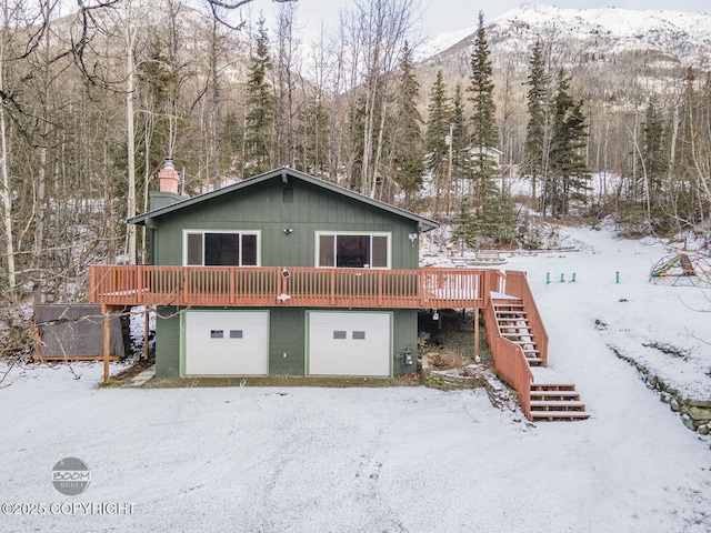 snow covered house with a deck with mountain view and a garage