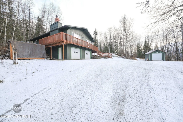 snow covered property featuring a deck, a garage, and an outbuilding