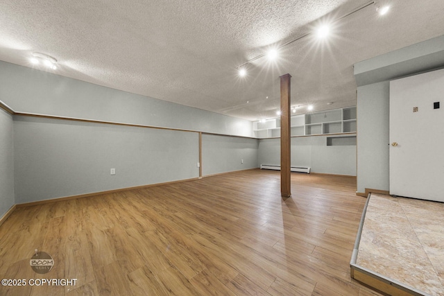 basement featuring rail lighting, hardwood / wood-style flooring, a textured ceiling, and a baseboard radiator