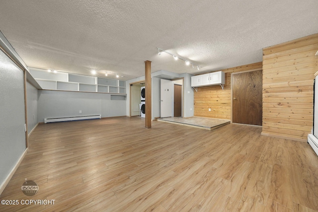 interior space with stacked washer / drying machine, a baseboard heating unit, wood walls, a wall mounted AC, and light hardwood / wood-style flooring