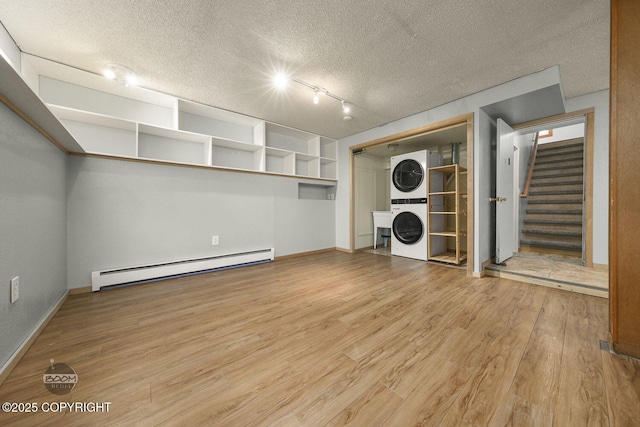 washroom featuring a textured ceiling, wood-type flooring, a baseboard heating unit, rail lighting, and stacked washing maching and dryer