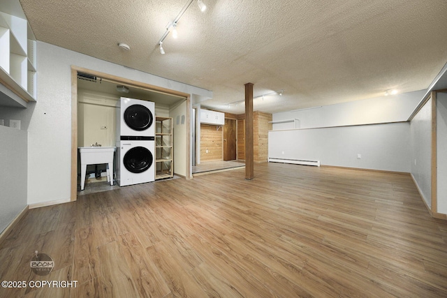 interior space featuring rail lighting, light hardwood / wood-style floors, a baseboard heating unit, a textured ceiling, and stacked washing maching and dryer