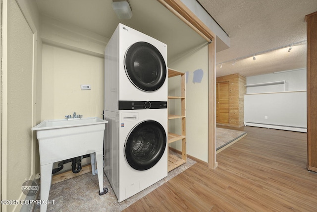 laundry room featuring stacked washer / drying machine, a baseboard heating unit, hardwood / wood-style flooring, a textured ceiling, and rail lighting