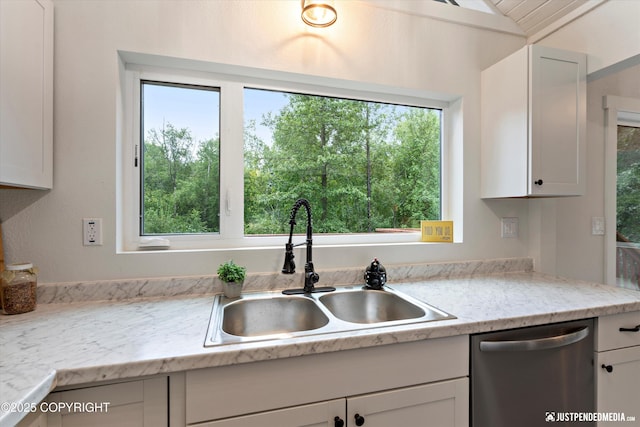 kitchen featuring stainless steel dishwasher, white cabinets, light stone counters, and sink