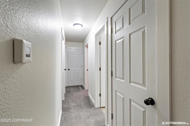 corridor with a textured ceiling and light colored carpet