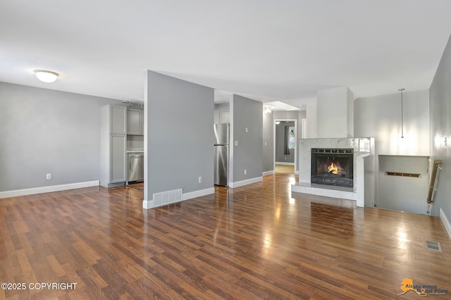 unfurnished living room featuring a tiled fireplace and dark wood-type flooring