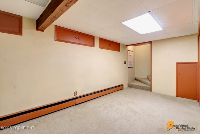 finished below grade area with baseboard heating, stairs, carpet flooring, and a paneled ceiling