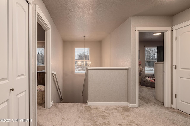 hall featuring light colored carpet, a notable chandelier, and a textured ceiling