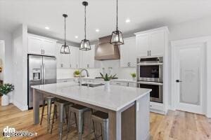 kitchen featuring white cabinets, custom range hood, stainless steel appliances, and a kitchen island with sink