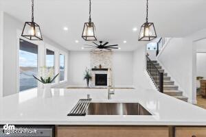 kitchen featuring decorative light fixtures, dishwashing machine, a large fireplace, and an island with sink