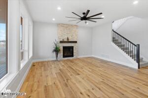 unfurnished living room with light wood finished floors, baseboards, stairway, a stone fireplace, and recessed lighting