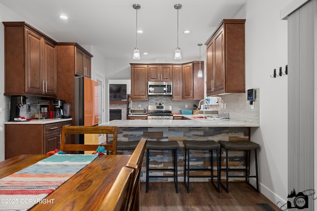 kitchen with tasteful backsplash, a breakfast bar area, dark hardwood / wood-style flooring, kitchen peninsula, and stainless steel appliances