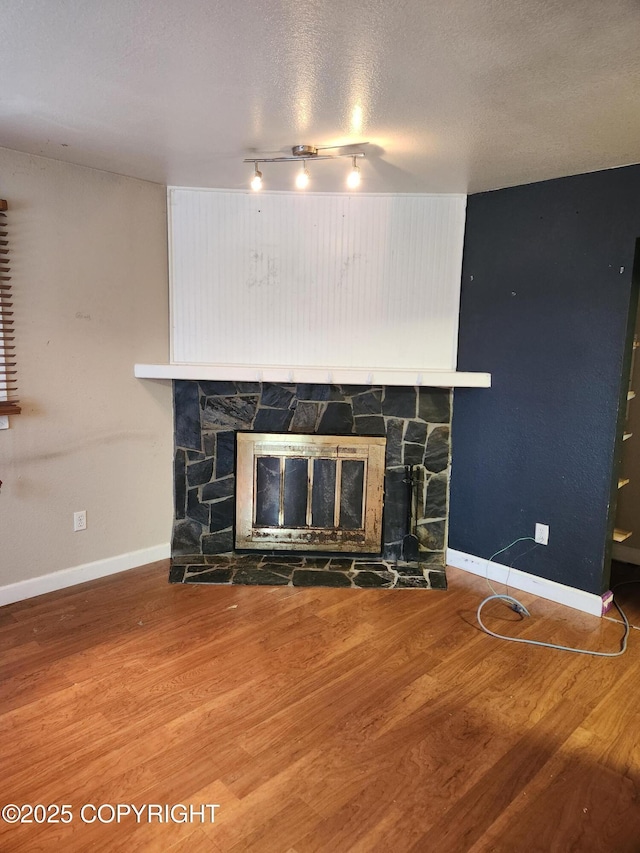 details featuring a stone fireplace, a textured ceiling, baseboards, and wood finished floors