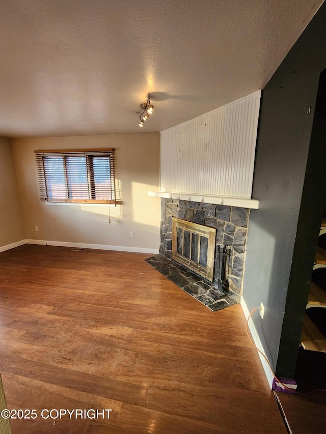 unfurnished living room featuring a fireplace, a textured ceiling, baseboards, and wood finished floors