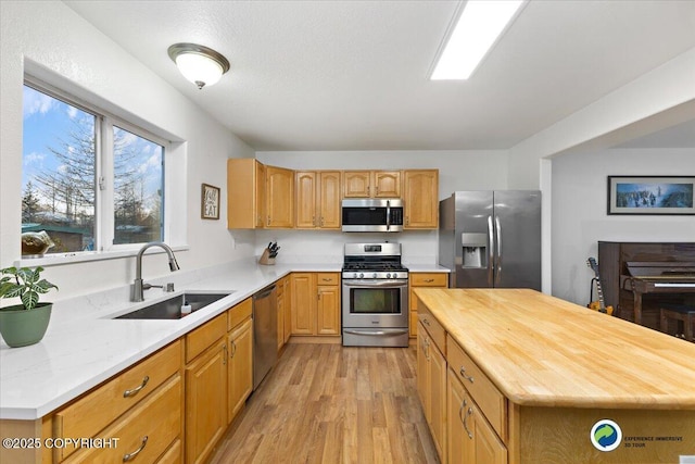 kitchen with sink, butcher block counters, stainless steel appliances, a kitchen island, and light wood-type flooring