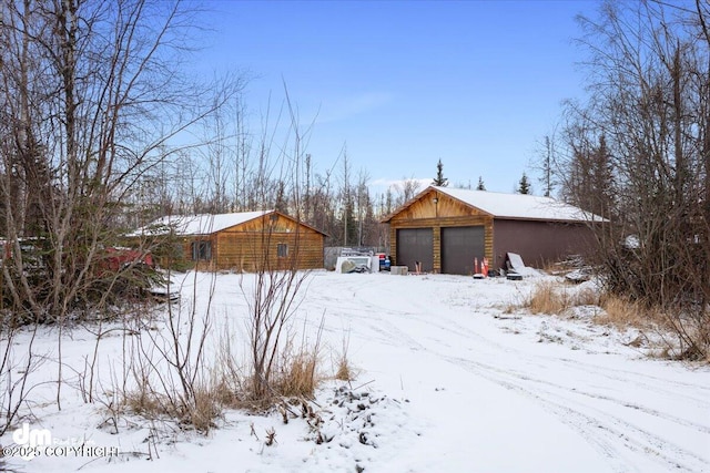 snowy yard with a garage and an outbuilding