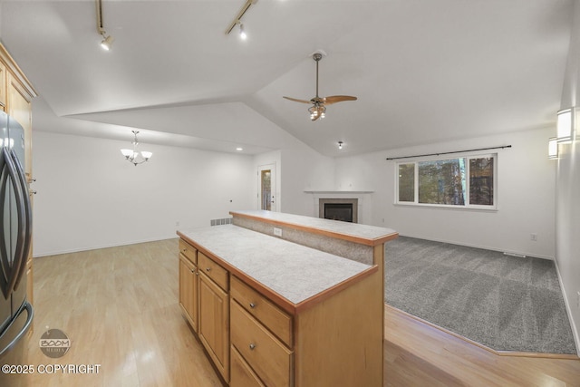 kitchen with a kitchen island, decorative light fixtures, vaulted ceiling, ceiling fan with notable chandelier, and stainless steel fridge