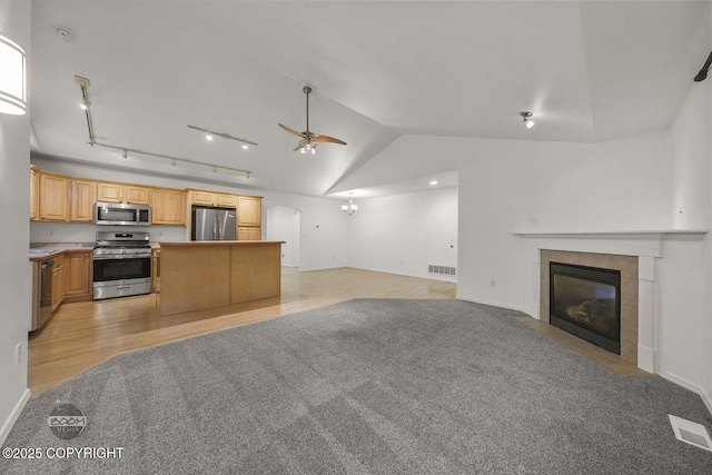 kitchen with ceiling fan with notable chandelier, appliances with stainless steel finishes, a kitchen island, light carpet, and a tiled fireplace