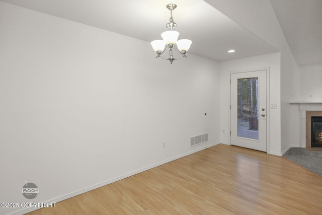 unfurnished living room with light hardwood / wood-style floors, a tile fireplace, and a chandelier