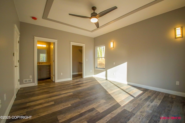 empty room with dark hardwood / wood-style floors, ceiling fan, and a tray ceiling