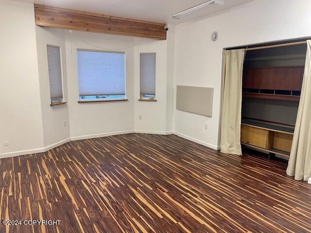 unfurnished room with dark hardwood / wood-style floors and beam ceiling