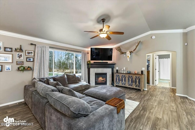 living room with a tile fireplace, vaulted ceiling, wood-type flooring, ceiling fan, and crown molding