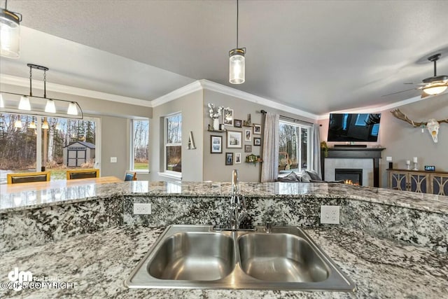 kitchen with sink, crown molding, a fireplace, stone countertops, and decorative light fixtures