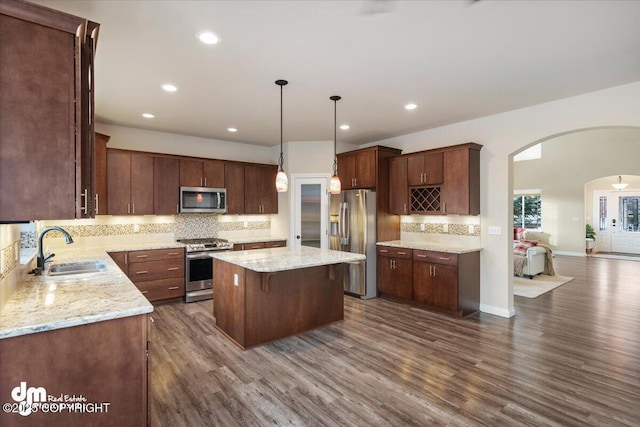 kitchen with sink, a kitchen island, decorative light fixtures, stainless steel appliances, and dark hardwood / wood-style flooring