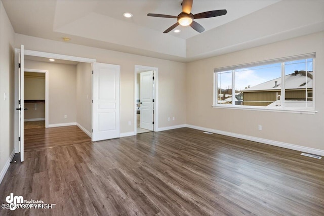 empty room with dark hardwood / wood-style flooring, ceiling fan, and a raised ceiling