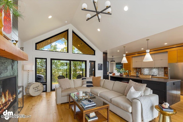 living room featuring light hardwood / wood-style floors, a tiled fireplace, high vaulted ceiling, and a notable chandelier