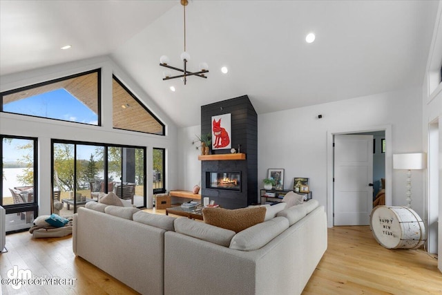 living room with a fireplace, high vaulted ceiling, light hardwood / wood-style flooring, and a notable chandelier