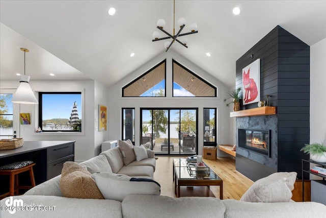 living room with a fireplace, high vaulted ceiling, light hardwood / wood-style flooring, and a notable chandelier