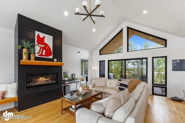 living room with a large fireplace, wood-type flooring, high vaulted ceiling, and a notable chandelier