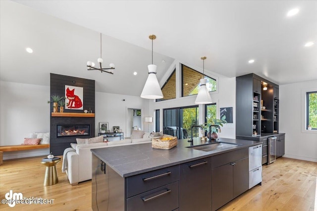 kitchen featuring sink, light wood-type flooring, pendant lighting, a fireplace, and a kitchen island with sink