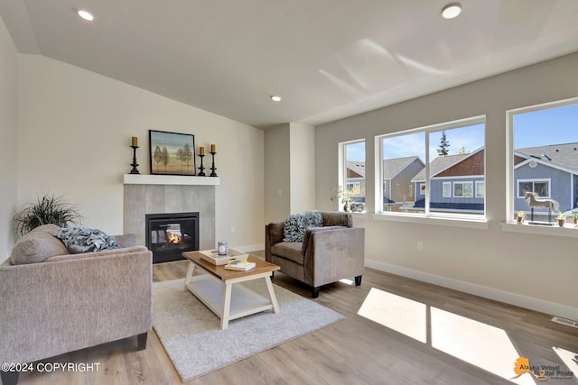 living room with a tile fireplace, vaulted ceiling, and hardwood / wood-style floors