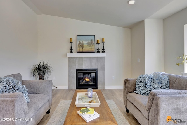 living room featuring lofted ceiling, hardwood / wood-style flooring, and a tile fireplace