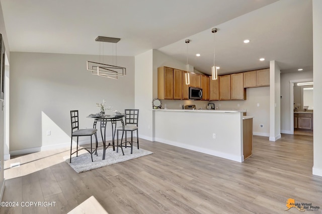 kitchen featuring lofted ceiling, hanging light fixtures, light hardwood / wood-style flooring, and kitchen peninsula