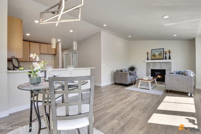 dining space with a tiled fireplace, lofted ceiling, and light hardwood / wood-style flooring