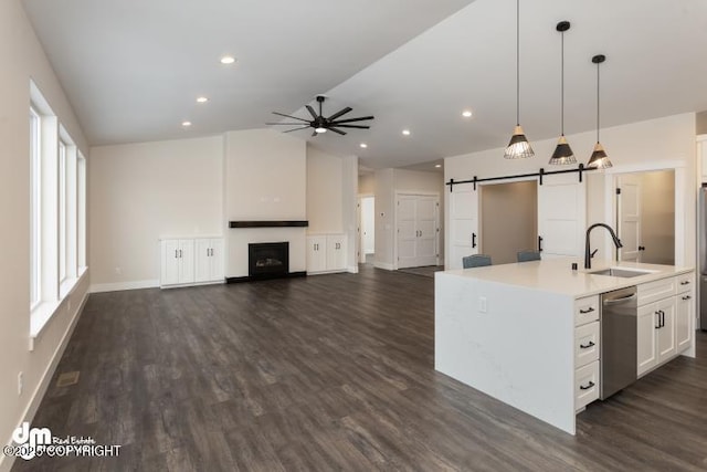 kitchen featuring sink, dishwasher, a center island with sink, decorative light fixtures, and a barn door